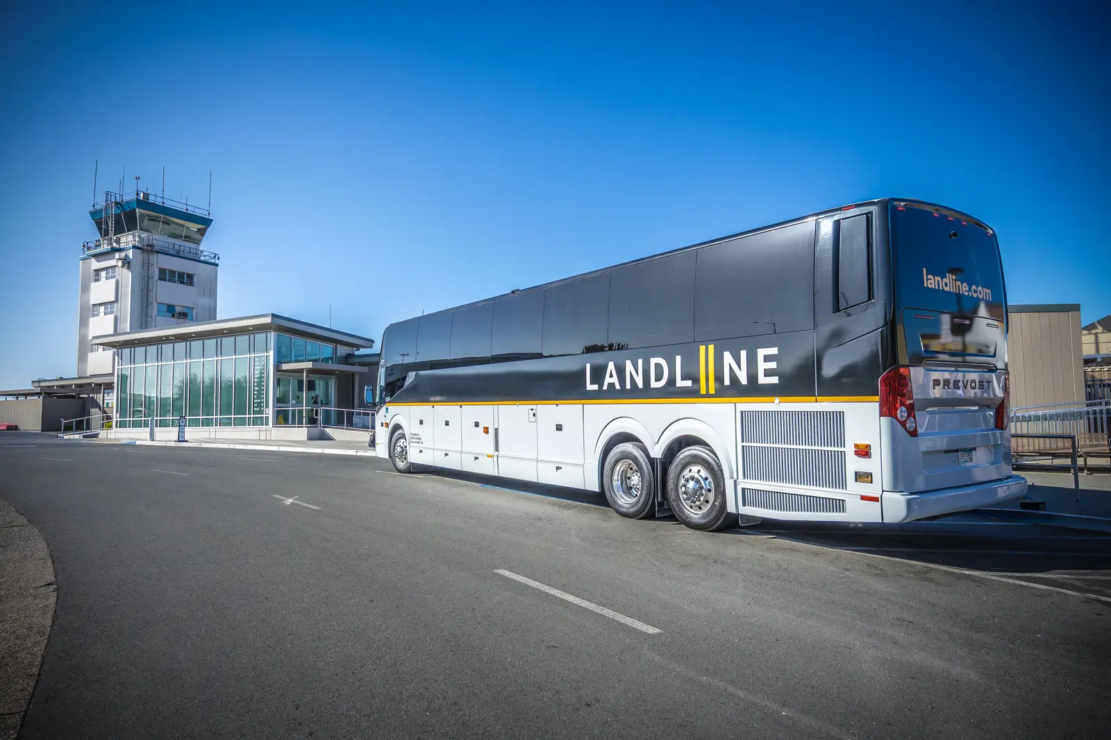 A Landline coach parked outside an airport terminal and control tower.